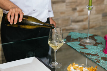 Chef pouring white wine into glass on restaurant table