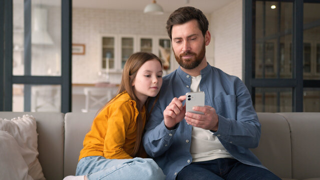 Positive joyful happy Caucasian family dad parent guy father celebrating man daughter win male using mobile phone success little child girl kid rejoicing victory online game victory cellphone at home