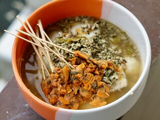 Authentic Lontong Kupang and Sate Kerang. A traditional clam soup with rice cakes in savory shrimp paste broth. Famous Indonesian street food specialty from Sidoarjo, East Java