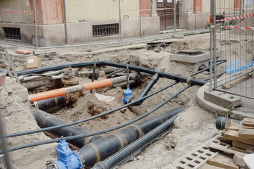 Road excavation exposing underground infrastructure, showing plastic and insulated pipes, gate...