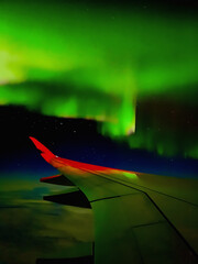 Breathtaking view of the Northern Lights (Aurora Borealis) seen from airplane window over Fairbanks, Alaska- Stunning aerial night sky phenomenon, glowing green waves above clouds.