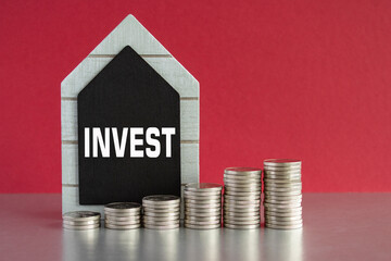invest symbol. Word invest written on a black board. Silver coins arranged in a graph in front....