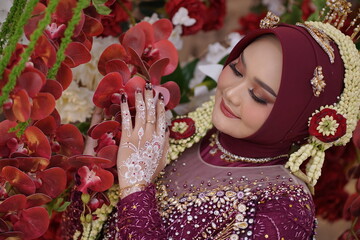 An elegant Muslim bride with white henna details gracefully touches red orchids, celebrating a...