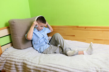 A boy in headphones listens to music from a smartphone while lying on the couch.