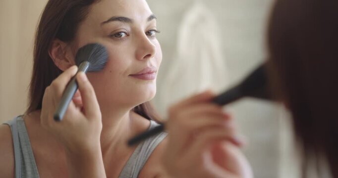 Young woman applying makeup to her face with a brush