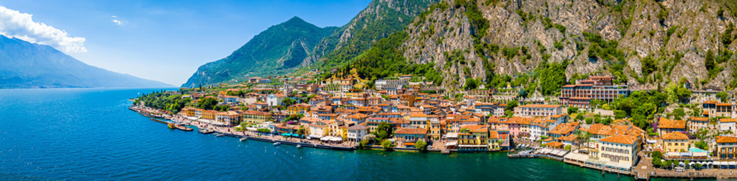 Aerial view of Limone sul Garda, a colorful lakeside town in Italy nestled between Lake Garda and steep mountains under a bright blue sky