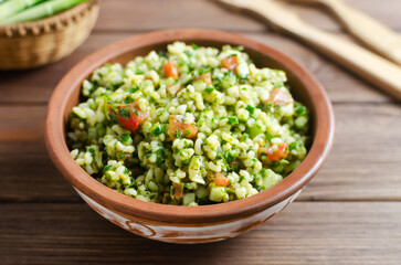 Oriental salad Tabbouleh in a ceramic bowl on a wooden table. Concept of traditional Lebanese or Syrian cuisine. Vegetarian or vegan dish. Rustic style. Selective focus. Horizontal orientation.