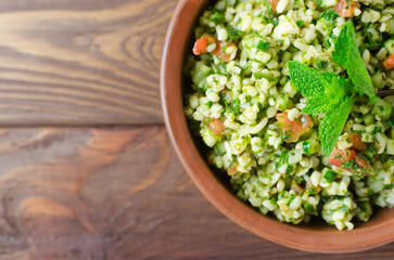 Oriental salad Tabbouleh in a ceramic bowl on a wooden table. Concept of traditional Lebanese or Syrian cuisine. Vegetarian or vegan dish. Selective focus. Horizontal orientation. Top view. Copy space
