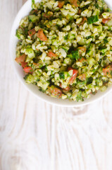 Oriental salad Tabbouleh in a white bowl on a wooden table. Concept of traditional Lebanese or Syrian cuisine. Vegetarian or vegan dish. Selective focus. Vertical orientation. Top view. Copy space