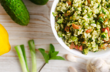 Oriental salad Tabbouleh in a white bowl on a wooden table. Concept of traditional Lebanese or Syrian cuisine. Vegetarian or vegan dish. Selective focus. Horizontal orientation. Top view