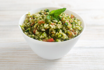 Oriental salad Tabbouleh in a white bowl on a wooden table. Concept of traditional Lebanese or Syrian cuisine. Vegetarian or vegan dish. Selective focus. Horizontal orientation.