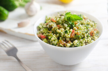 Oriental salad Tabbouleh in a white bowl on a wooden table. Concept of traditional Lebanese or Syrian cuisine. Vegetarian or vegan dish. Selective focus. Horizontal orientation. Copy space