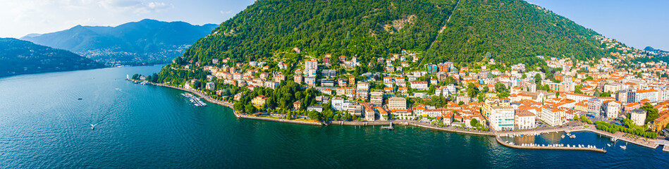 Fototapeta premium Aerial summer view of Lake Como with deep blue water, surrounding green hills, villas, and boats under a clear, sunny sky in Italy