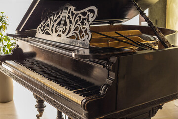 Side view of a vintage grand piano with an ornate decorative music stand and open lid, photographed in natural light.