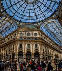 Naklejka premium Interior view of Galleria Vittorio Emanuele II in Milan with glass dome, ornate facades, and decorative fresco under bright daylight