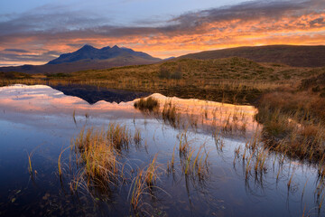 Black Cuillin mountains reflecting in calm loch at sunset near Sligachan on The Isle of Skye, Scotland, UK.