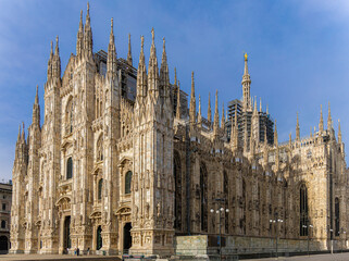 Gothic-style Milan Cathedral facade with ornate spires and intricate stonework against clear blue...