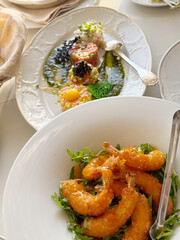 Plate of crispy, breaded fried shrimp served on a bed of fresh arugula, with metal tongs, ideal for...