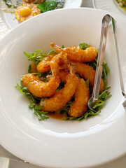 Plate of crispy, breaded fried shrimp served on a bed of fresh arugula, with metal tongs, ideal for culinary, seafood, or restaurant menu designs