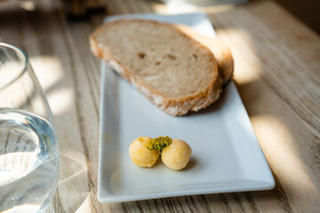 Zwei Scheiben Brot mit Kräuterbutter auf einem weißen Teller, neben einem Glas Wasser auf Holztisch