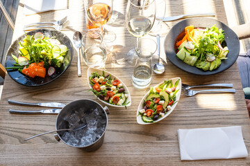 Ein Tisch gedeckt mit frischen Salaten, Wein, Wasser und Eis, bereit für ein sommerliches Essen