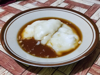 Bubur sumsum, traditional Indonesian food. Soft white marrow porridge served on a plate sprinkled with thick brown sugar sauce on a wooden patterned table.
