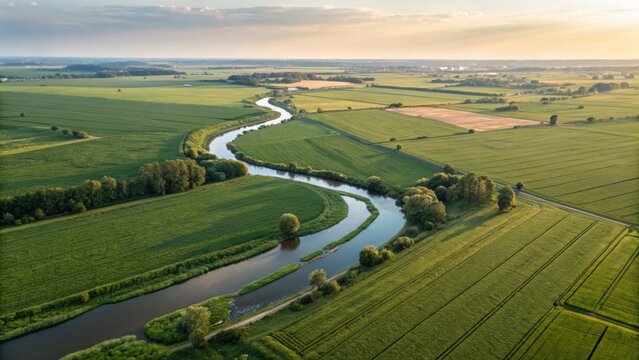 Aerial view of winding river through green fields at sunset, showcasing rural landscape