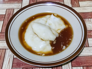 Bubur sumsum, traditional Indonesian food. Soft white marrow porridge served on a plate sprinkled with thick brown sugar sauce on a wooden patterned table.