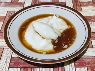 Bubur sumsum, traditional Indonesian food. Soft white marrow porridge served on a plate sprinkled with thick brown sugar sauce on a wooden patterned table.