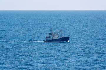 Fishing boat in blue sea and clear sky with birds flying overhead.