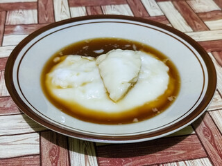 Bubur sumsum, traditional Indonesian food. Soft white marrow porridge served on a plate sprinkled with thick brown sugar sauce on a wooden patterned table.