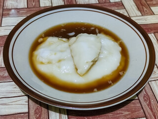 Bubur sumsum, traditional Indonesian food. Soft white marrow porridge served on a plate sprinkled with thick brown sugar sauce on a wooden patterned table.