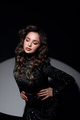 A girl in a black dress sits on a chair, she has curly hair