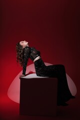 Girl in long black dress near white cube on red background