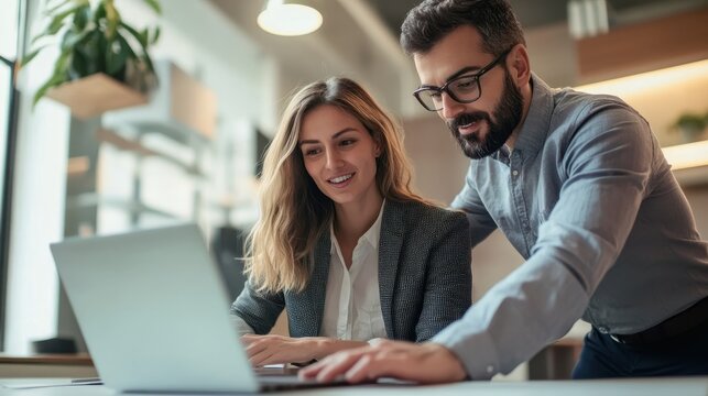 Teaching moment between businesswoman and young employee with laptop in office, highlighting mentorship and teamwork in modern professional environment with text-ready background