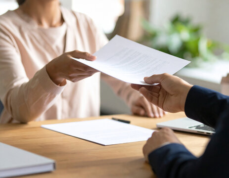 Two individuals exchanging documents across a wooden desk symbolizing a business transaction or important discussion