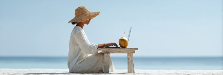 Young woman wearing a straw hat enjoys working remotely on her laptop while sitting at a wooden table on a beautiful beach with a refreshing coconut drink, embracing the digital nomad lifestyle