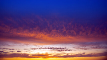 Dramatic sunset sky featuring golden, fiery clouds against a deepening blue background. The rich colors and dynamic cloud formations create a stunning natural display.