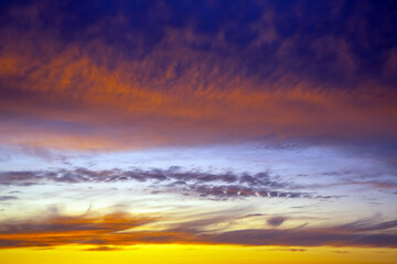 Dramatic sunset sky featuring golden, fiery clouds against a deepening blue background. The rich colors and dynamic cloud formations create a stunning natural display.