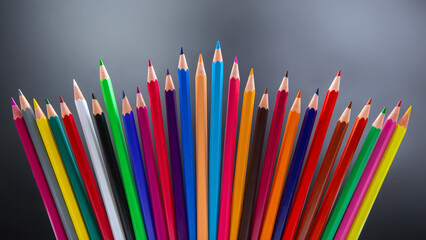 A vibrant row of colored pencils in various shades, standing upright against a blurred gray background. Perfect for art, education, and creativity themes.