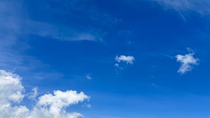 Mostly clear bright blue sky with scattered small white clouds. Perfect for background use in designs, presentations, websites, and social media posts.