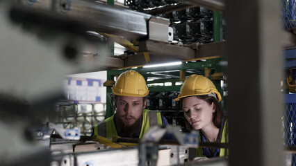 Two factory workers in safety vests and helmets examine auto parts assembly inside an automotive manufacturing plant, highlighting teamwork and mechanical precision.