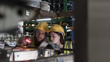Male and female workers scan barcodes on machinery in automotive manufacturing facility, confirming part tracking and data accuracy under modern industrial system.
