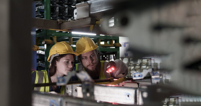 Male and female workers scan barcodes on machinery in automotive manufacturing facility, confirming part tracking and data accuracy under modern industrial system.