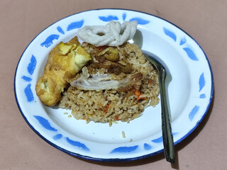 Fried rice with omelet, chicken pieces and red chili slices, has a delicious taste, served on a classic iron plate, with a brown background.