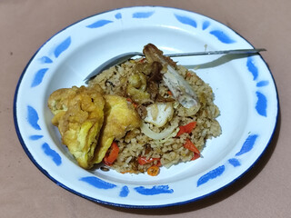Fried rice with omelet, chicken pieces and red chili slices, has a delicious taste, served on a classic iron plate, with a brown background.