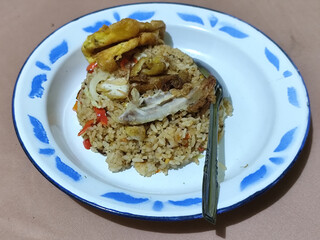 Fried rice with omelet, chicken pieces and red chili slices, has a delicious taste, served on a classic iron plate, with a brown background.