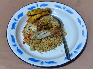 Fried rice with omelet, chicken pieces and red chili slices, has a delicious taste, served on a classic iron plate, with a brown background.