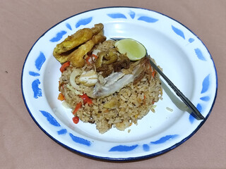 Fried rice with omelet, chicken pieces and red chili slices, has a delicious taste, served on a classic iron plate, with a brown background.