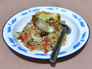 Fried rice with omelet, chicken pieces and red chili slices, has a delicious taste, served on a classic iron plate, with a brown background.